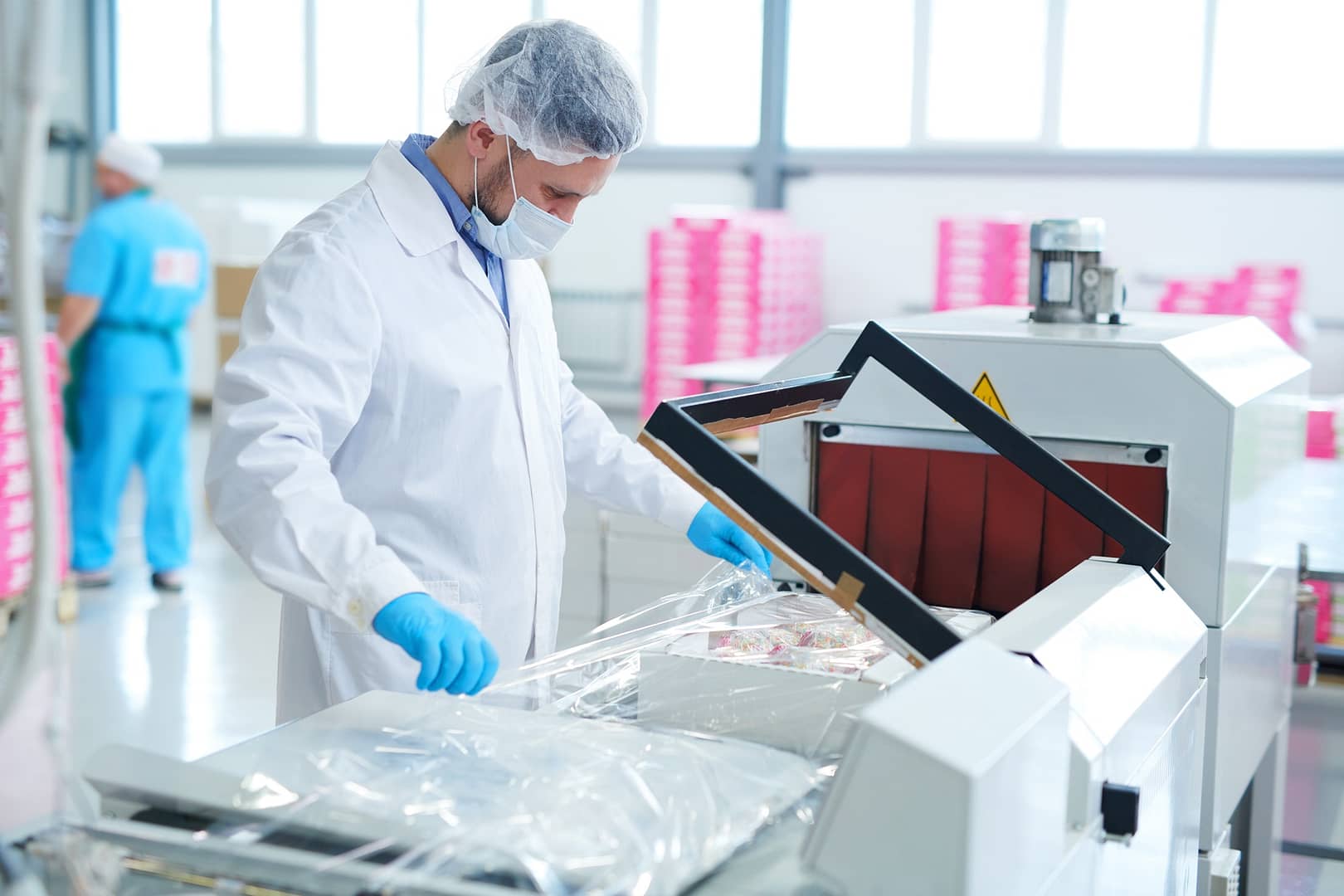 Confectionery factory worker packing box into plastic film