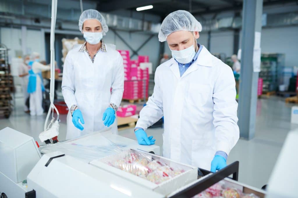 Confectionery factory employees packing boxes into plastic film